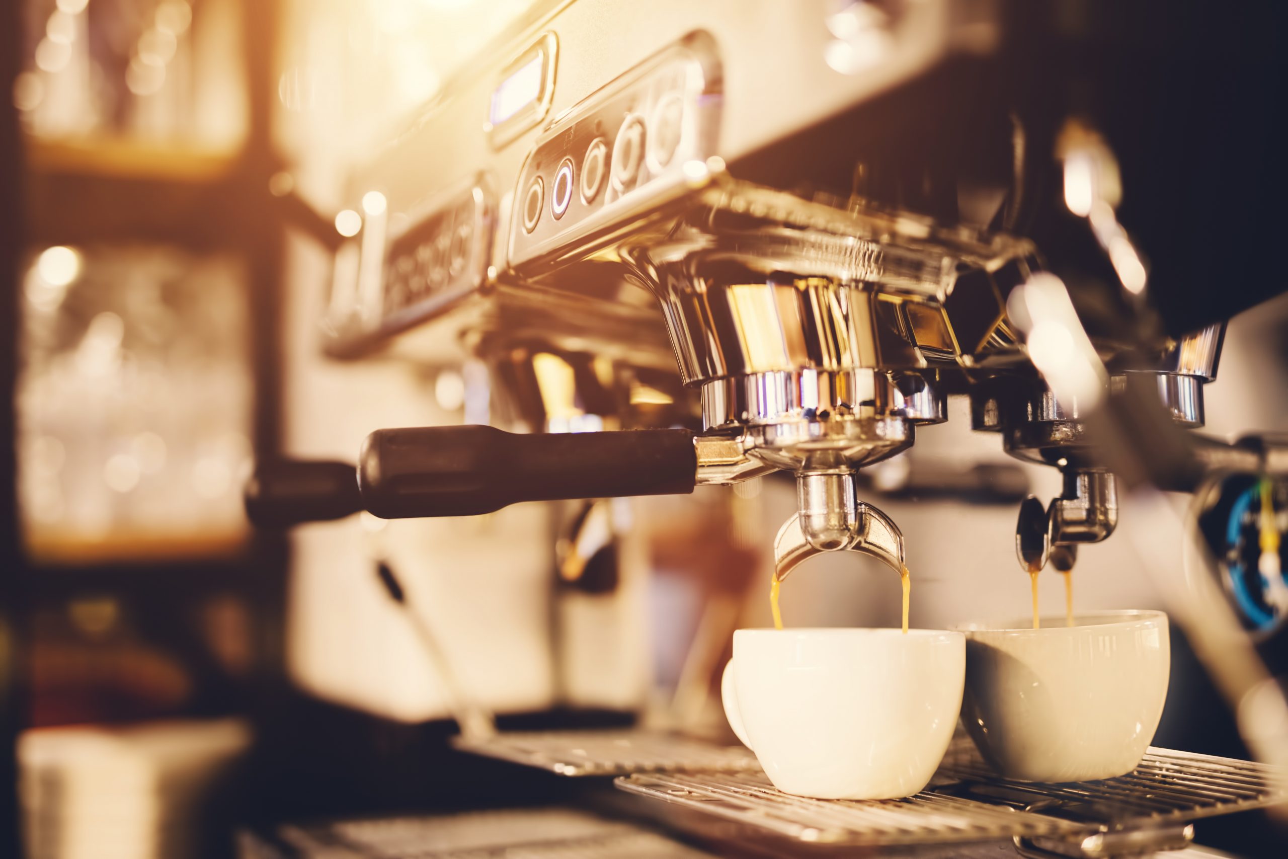 White cup standing beneath a coffeemaker, coffee pouring into it. Morning beverage preparation.